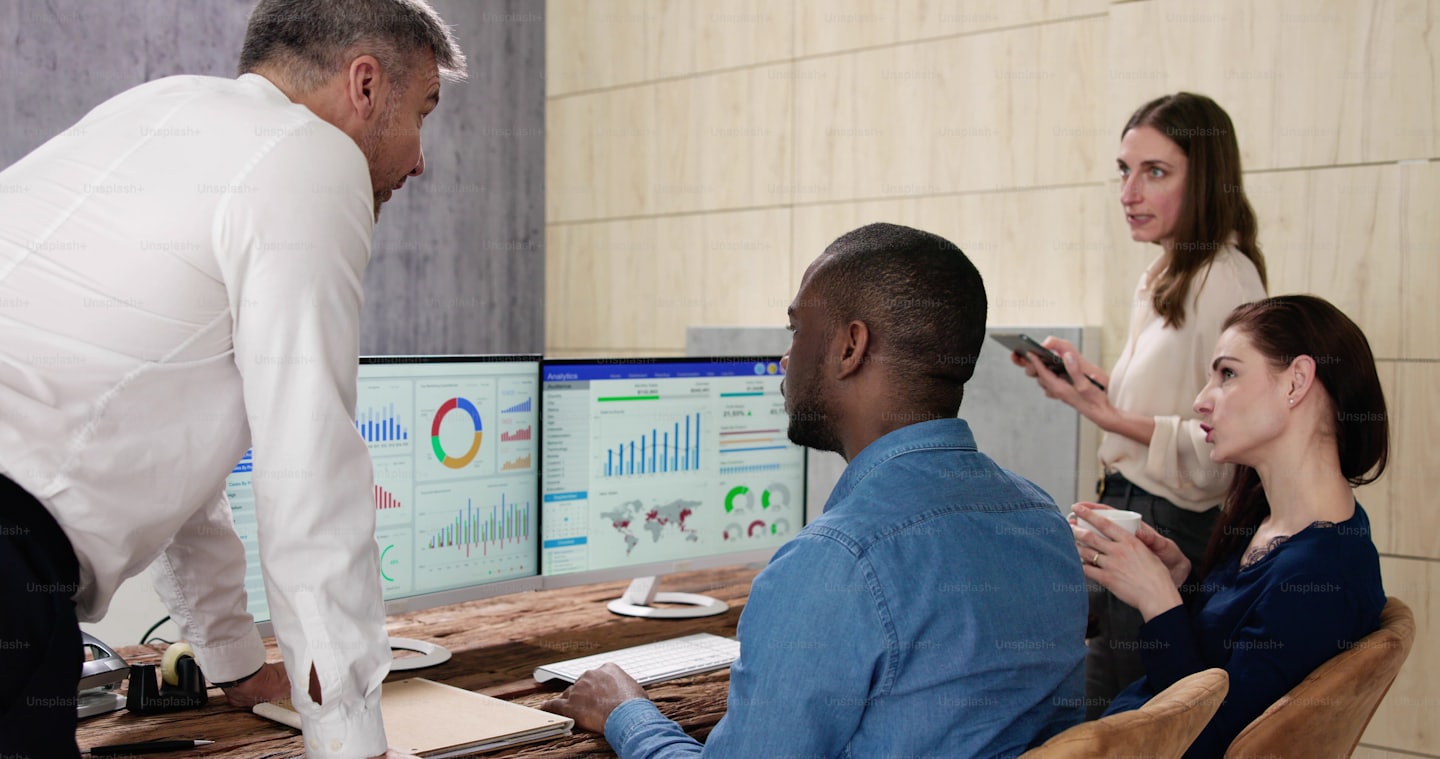 Profesionales de negocios colaboran analizando datos en monitores de computadora.